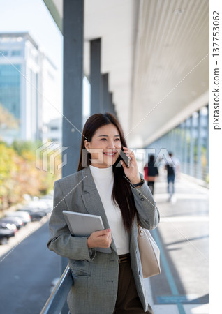 Asian woman student office worker talking on phone holding tablet as standing walking on footbridge. 137753062