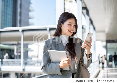 Pretty asian woman student office worker holding tablet looking at phone and standing on footbridge. Pretty asian woman student office worker holding tablet looking at phone and standing on footbridge. 137753064