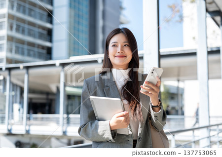 Pretty asian woman student office worker holding tablet and phone standing on bridge with cityscape. 137753065