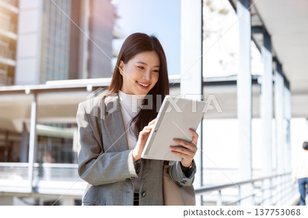 Pretty asian woman student or office worker looking at tablet standing on footbridge with cityscape. Pretty asian woman student or office worker looking at tablet standing on footbridge with cityscape. 137753068