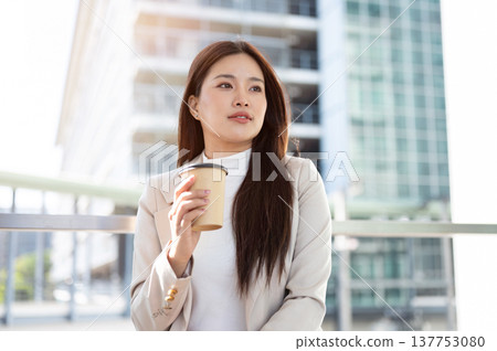 Pretty asian woman office worker holding coffee cup standing aside railing on bridge with cityscape. Pretty asian woman office worker holding coffee cup standing aside railing on bridge with cityscape. 137753080
