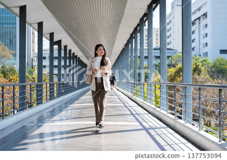 Happy asian woman office worker holding coffee walking with hand in pocket in sunlight on footbridge Happy asian woman office worker holding coffee walking with hand in pocket in sunlight on footbridge 137753094