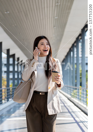Happy asian woman office worker holding coffee talking on phone while walking standing on footbridge 137753100