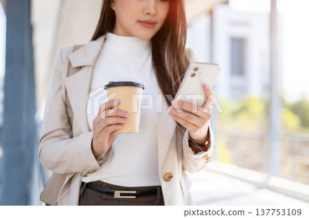 Close up of asian woman office worker holding coffee looking at phone standing walking on footbridge 137753109