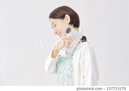 Woman wearing an apron using a massage gun, stiff shoulders, white background 137753270