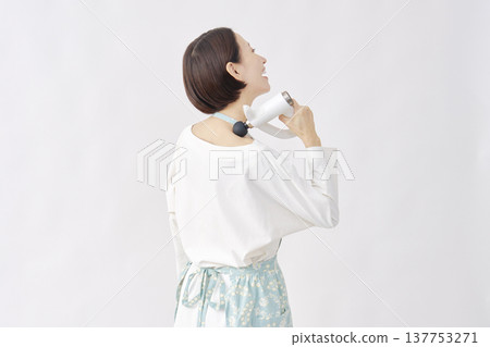 一位身穿圍裙的女子正在使用按摩槍，她肩膀僵硬，背景為白色。 137753271