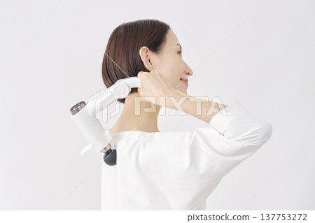 一位女士正在使用按摩槍，她的肩膀僵硬，背景為白色。 137753272