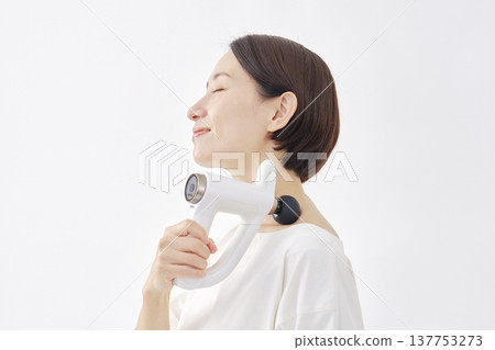 一位女士正在使用按摩槍，她的肩膀僵硬，背景為白色。 137753273