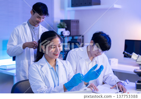 Asian woman scientist researcher wearing rubber gloves before working with colleague at table in lab 137753388