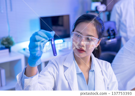 Asian woman scientist researcher holding test tube and looking at liquid while working in lab room. Asian woman scientist researcher holding test tube and looking at liquid while working in lab room. 137753393