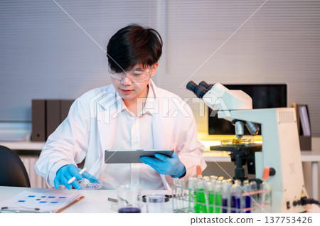 Asian man scientist researcher holding tablet looking at plant test sample at work table in lab room Asian man scientist researcher holding tablet looking at plant test sample at work table in lab room 137753426