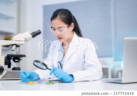 Woman scientist researcher using magnifying glass looking at test sample while working in lab room. Woman scientist researcher using magnifying glass looking at test sample while working in lab room. 137753438