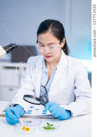 Woman scientist researcher using magnifying glass looking at test sample while working in a lab room Woman scientist researcher using magnifying glass looking at test sample while working in a lab room 137753439