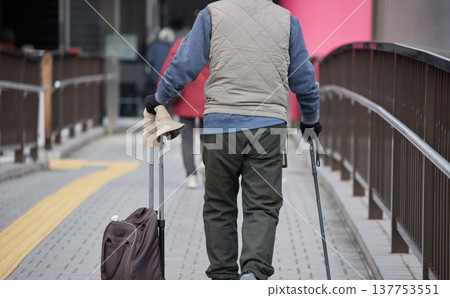 A senior man crosses a pedestrian overpass in a city during the daytime in winter. 137753551