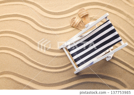 A lounge chair sits in warm sand next to a pair of sandals A lounge chair sits in warm sand next to a pair of sandals 137753985
