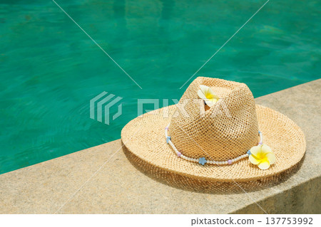 A straw hat with flowers rests near a clear pool A straw hat with flowers rests near a clear pool 137753992
