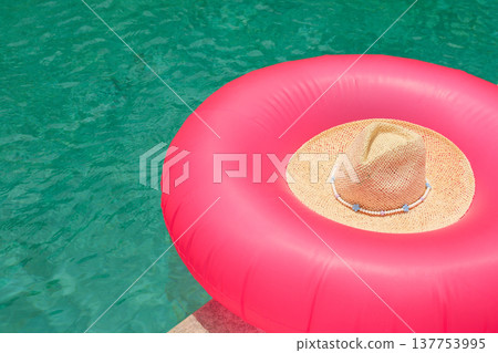 A pink float with a straw hat rests by clear water A pink float with a straw hat rests by clear water 137753995