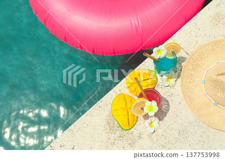 Two colorful drinks sit by the pool with a float nearby 137753998