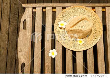 A sunhat sits on a wooden table with flowers beside it 137753999