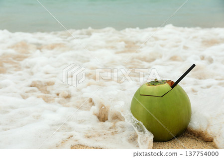A coconut drink sits on the sand near the ocean waves 137754000