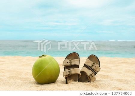 Coconut and sandals sit on the sandy beach in Bali Coconut and sandals sit on the sandy beach in Bali 137754003