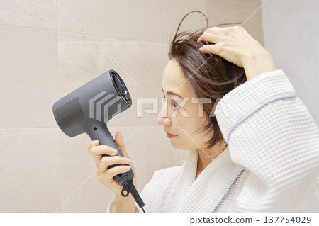 A woman drying her hair with a dryer. A woman drying her hair with a dryer. 137754029