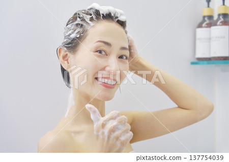 一位女士一邊洗頭一邊微笑，豎起了大拇指。 137754039