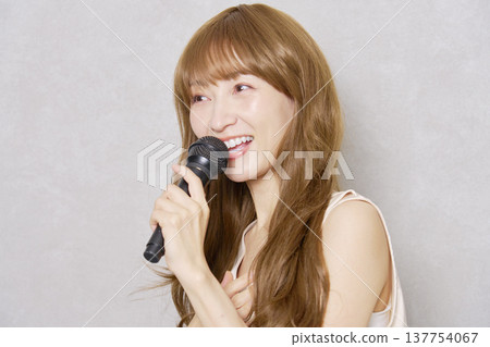 Middle-aged woman singing with a microphone, portrait, gray background Middle-aged woman singing with a microphone, portrait, gray background 137754067