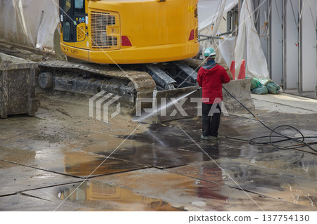A worker cleaning heavy machinery at a construction site. A worker cleaning heavy machinery at a construction site. 137754130