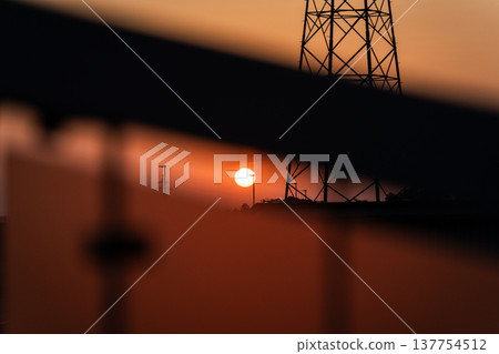 Sunset and transmission towers visible from a pedestrian overpass in the city. Sunset and transmission towers visible from a pedestrian overpass in the city. 137754512