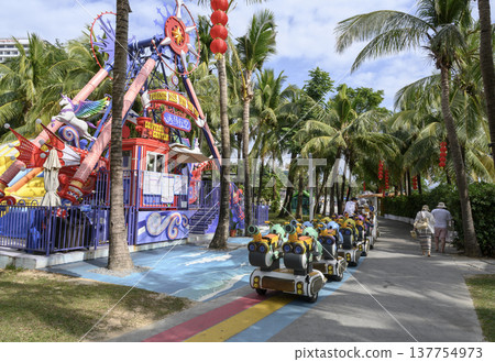A park with tropical palm trees, a children's train and attractions in China 137754973