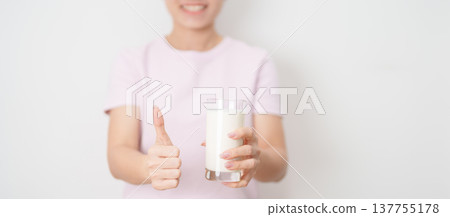 Healthy woman with glass of fresh milk and show thumbs up at home, female drinking for calcium and strong bones, high protein, dairy product for healthy lifestyle, wellness and daily routine concept 137755178
