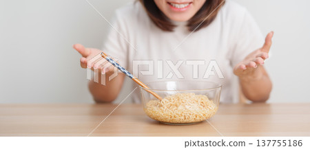 Happy young Asian woman enjoying a delicious bowl of hot instant noodles while relaxing at home, Cheerful female eating instant ramen with a smile at apartment. Simple lifestyle and quick meal concept 137755186