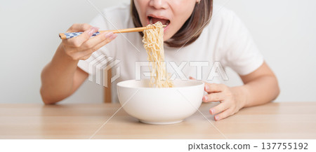 Happy young Asian woman enjoying a delicious bowl of hot instant noodles while relaxing at home, Cheerful female eating instant ramen with a smile at apartment. Simple lifestyle and quick meal concept Happy young Asian woman enjoying a delicious bowl of hot instant noodles while relaxing at home, Cheerful female eating instant ramen with a smile at apartment. Simple lifestyle and quick meal concept 137755192