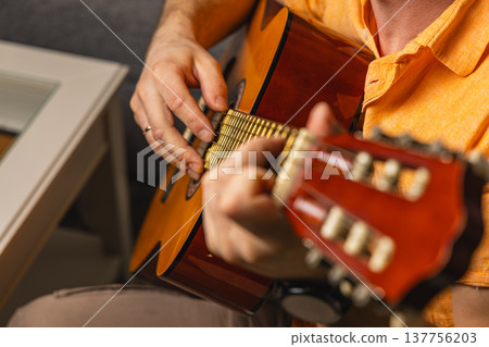 Person plays guitar in a cozy indoor setting during the day Person plays guitar in a cozy indoor setting during the day 137756203
