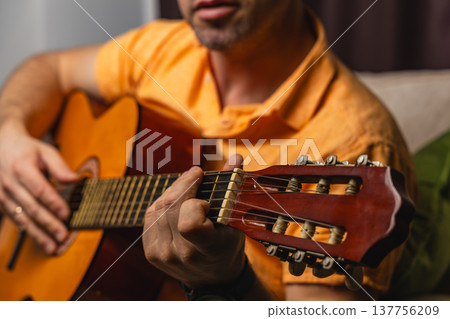 Man plays guitar at home during evening hours with focus on hands Man plays guitar at home during evening hours with focus on hands 137756209