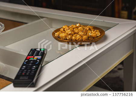 Bowl of popcorn on a table next to a remote control in a home setting Bowl of popcorn on a table next to a remote control in a home setting 137756216
