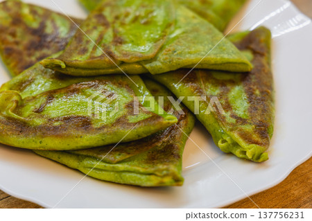 Freshly cooked green pancakes on a white plate at a kitchen table 137756231