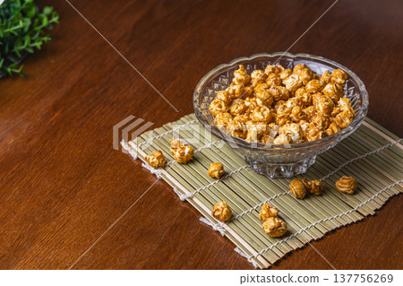 Caramel popcorn in a clear bowl on a wooden surface with a mat Caramel popcorn in a clear bowl on a wooden surface with a mat 137756269