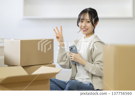 A smiling young woman sits surrounded by cardboard boxes, looking directly at the camera. (Image: Moving) A smiling young woman sits surrounded by cardboard boxes, looking directly at the camera. (Image: Moving) 137756560