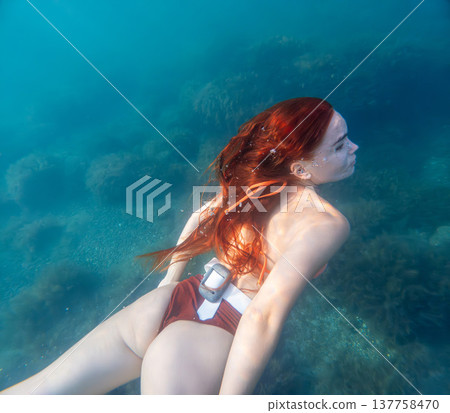 Woman diving redhead young woman with long red hair swimming underwater in clear blue ocean water during a serene summer vacation Woman diving redhead young woman with long red hair swimming underwater in clear blue ocean water during a serene summer vacation 137758470