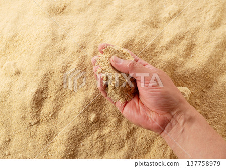 The image shows someone picking up rice bran with their hands to feel its texture. 137758979
