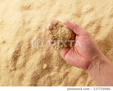 The image shows someone picking up rice bran with their hands to feel its texture. 137758980