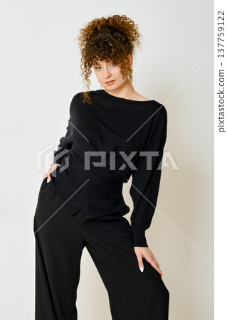 Fashion model showcases stylish black outfit in studio setting during daytime Fashion model showcases stylish black outfit in studio setting during daytime 137759122