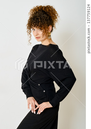 Stylish woman poses confidently in black outfit with unique design and curly hair Stylish woman poses confidently in black outfit with unique design and curly hair 137759124