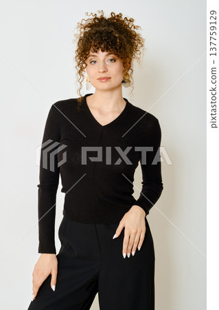 Model wearing black sweater poses against a plain wall showcasing spring fashion trends 137759129