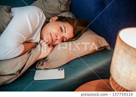 Tired middle aged woman sleeping in bed after using smartphone. Tired middle aged woman sleeping in bed after using smartphone. 137759319