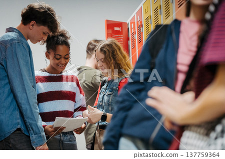 Teen students hanging out in school hallway by lockers, looking at project. Teen students hanging out in school hallway by lockers, looking at project. 137759364