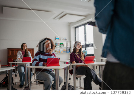 Teen student listening attentively during class while using digital tablet. Teen student listening attentively during class while using digital tablet. 137759383