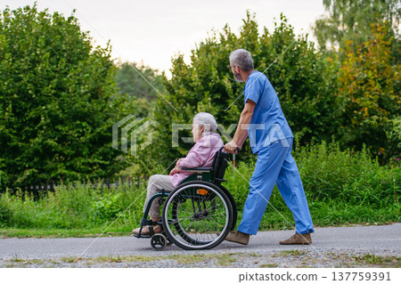 Senior patient and male nurse talking during walk outdoors. 137759391